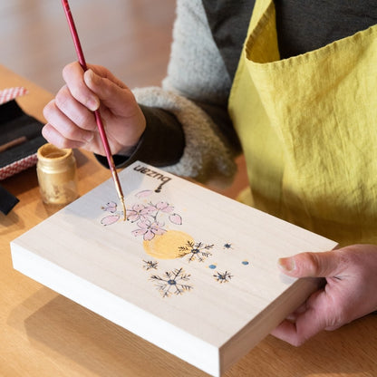 Close-up of a Buzan Kiln artisan painting sakura and gold leaf design on a wooden box, expressing the refined beauty of traditional Japanese craftsmanship.