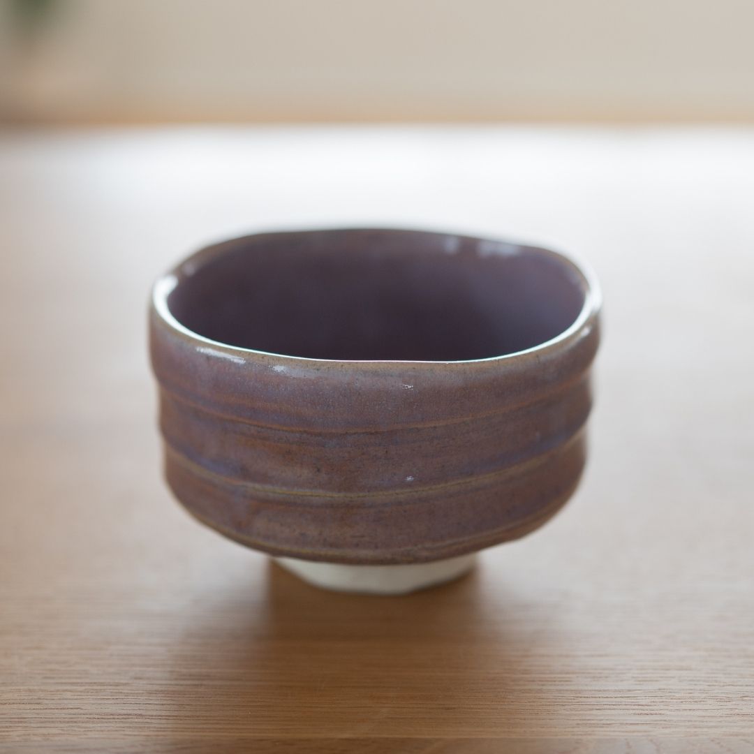 Detailed texture of a Japanese matcha bowl in Pale Violet Mino Ware, highlighting the Shino clay peeking through the flowing light purple glaze, characteristic of the Shinzan Kiln chawan.