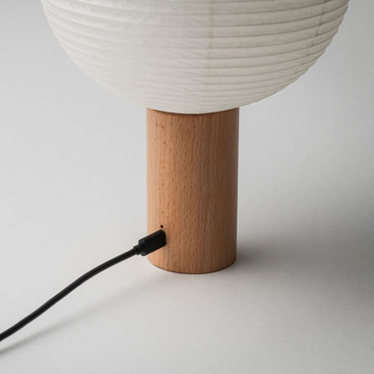 A portable paper lamp with a wooden base featuring a charging port, connected to a charging cable