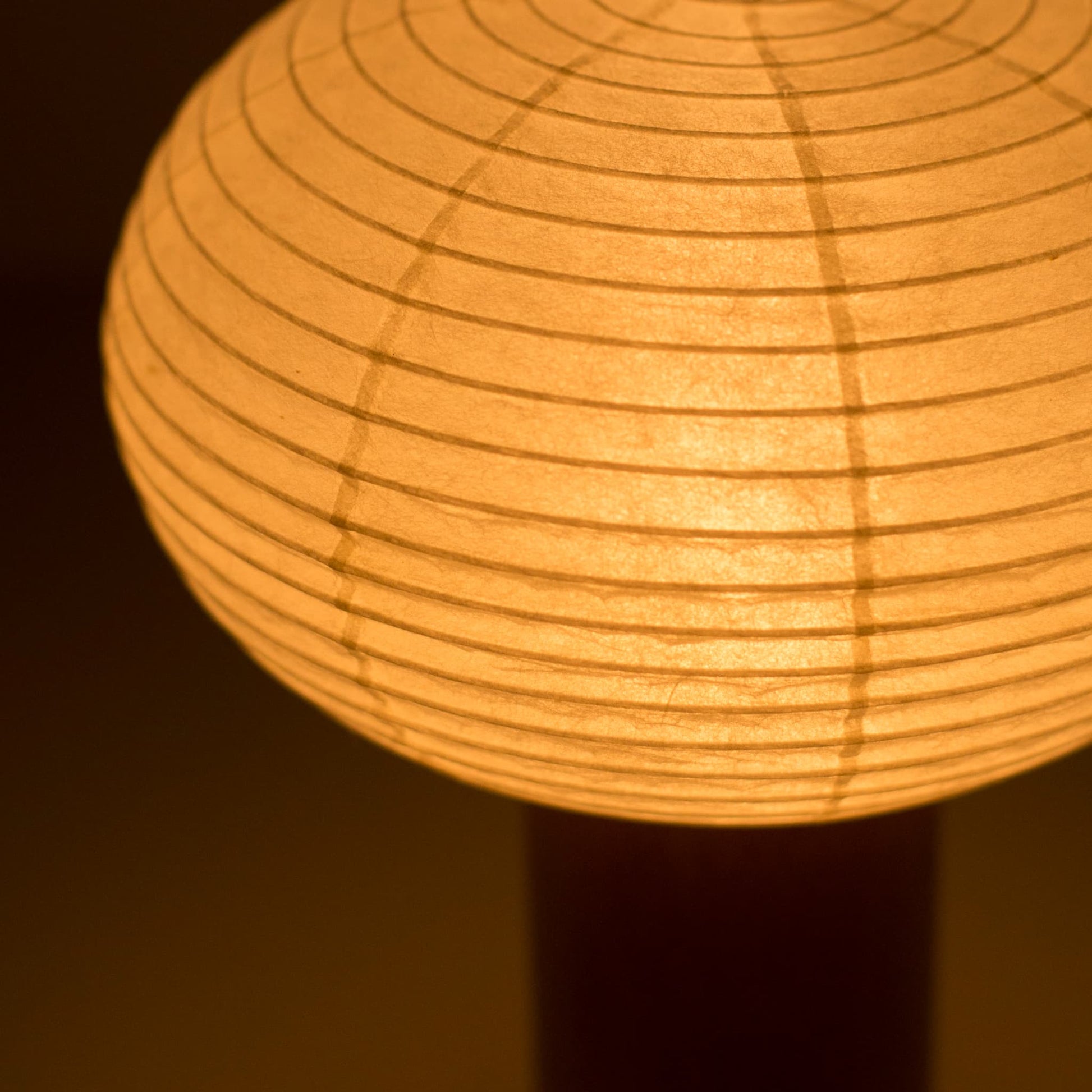 Close-up of the "TORCHIN OVAL"  portable paper lamp, emphasizing the delicate craftsmanship of the washi paper shade and the warm light it emits.