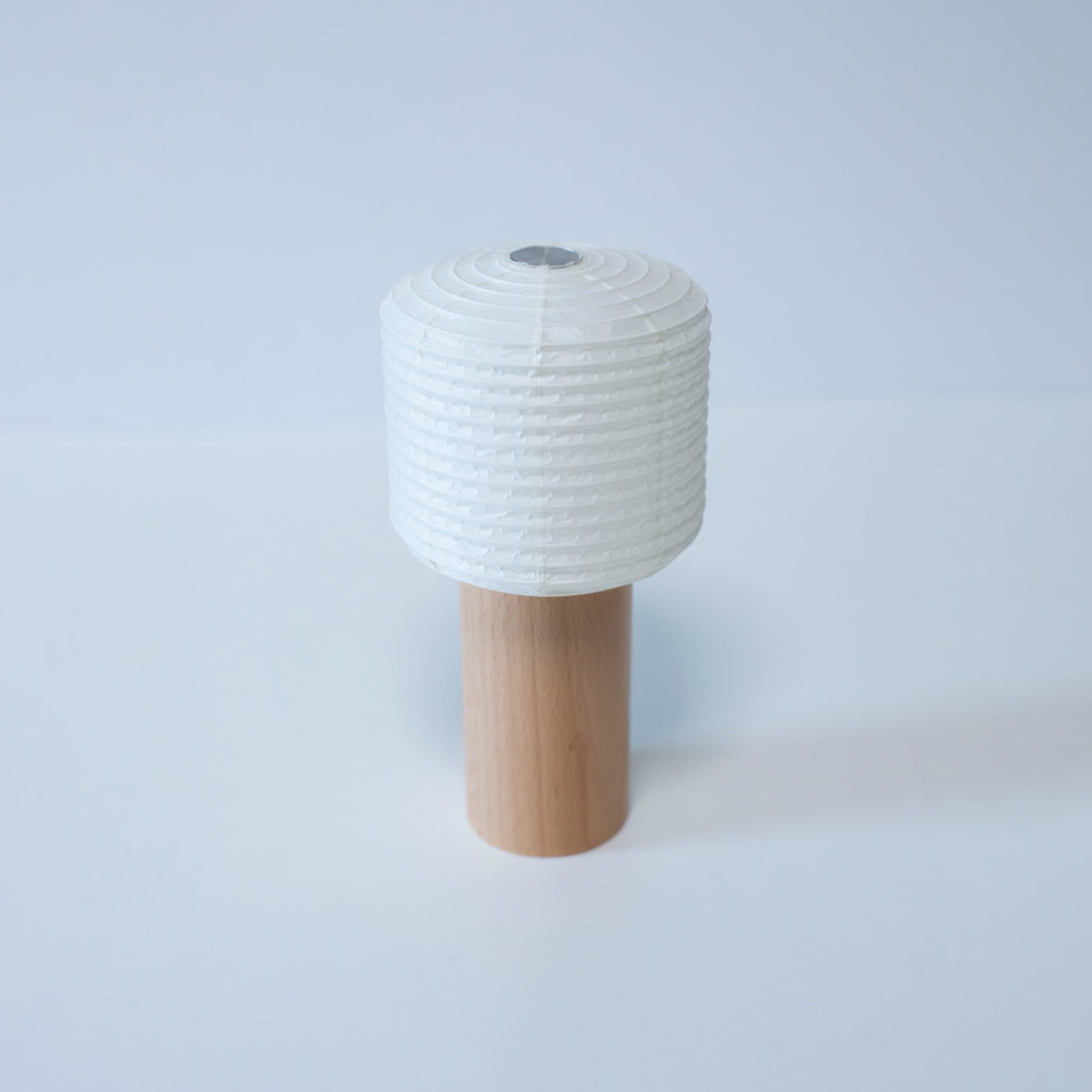 A portable paper lamp with a small paper top and wooden handle against a bright white background