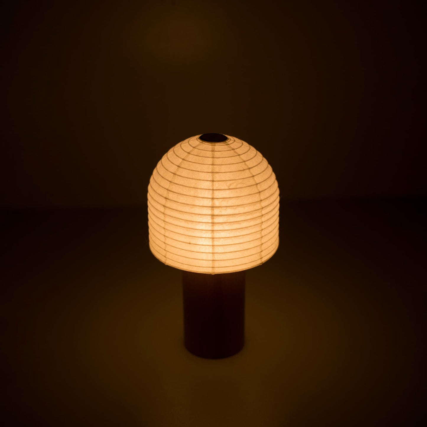 A portable Yame lantern with a wooden handle and bell-shaped cylindrical paper top emitting warm light in a dark room