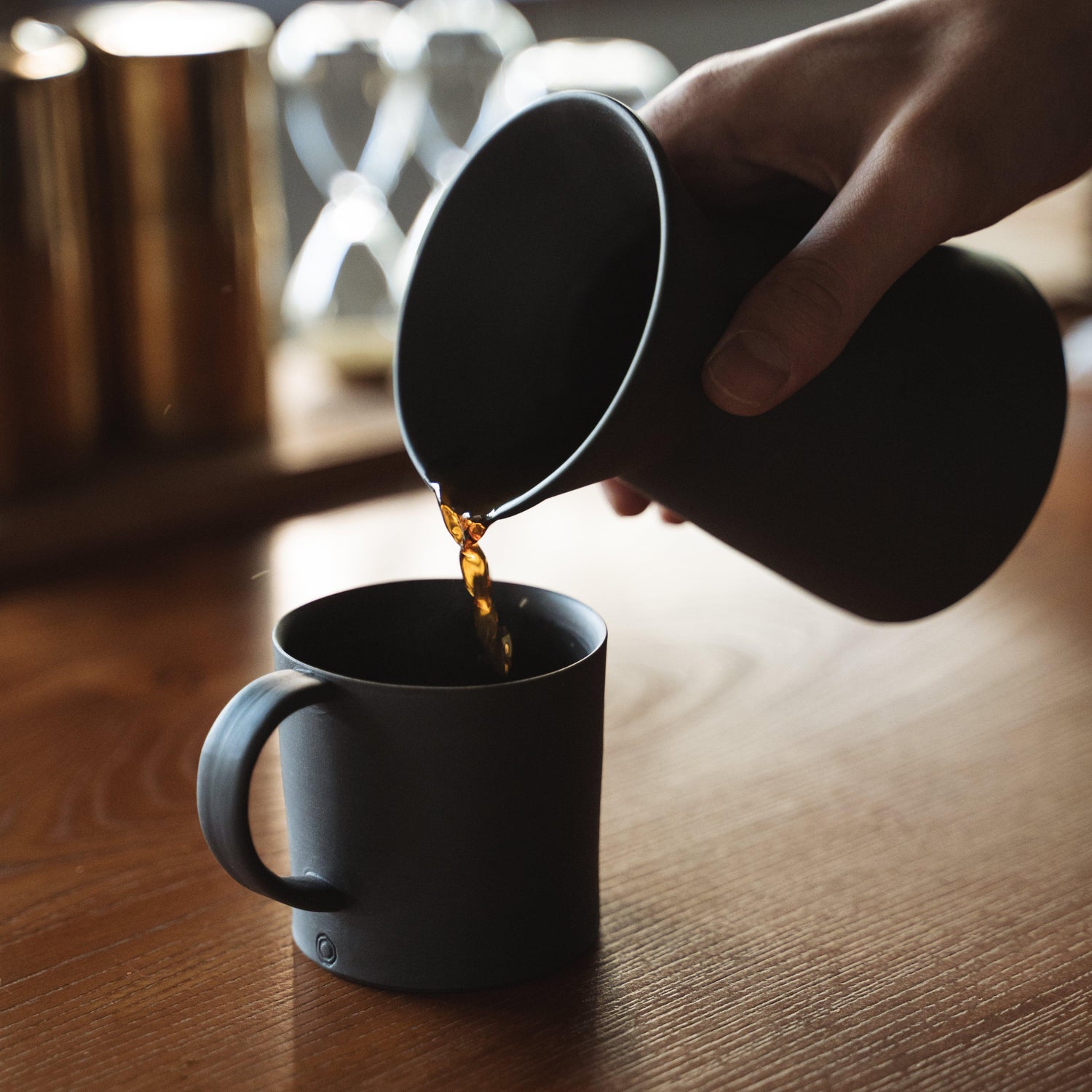 Pouring coffee from a minimalist black Banko ware coffee server into a black mug.