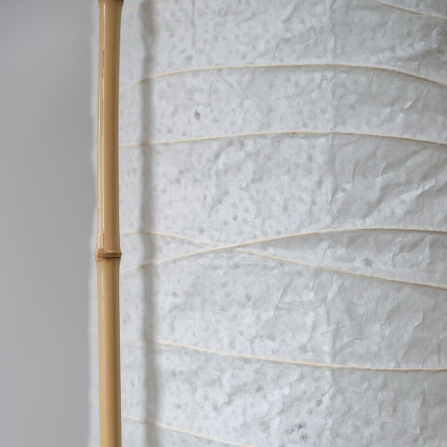 Detailed side view of a cylindrical Japanese lamp, showing the contrast between soft white washi paper and brown bamboo frame