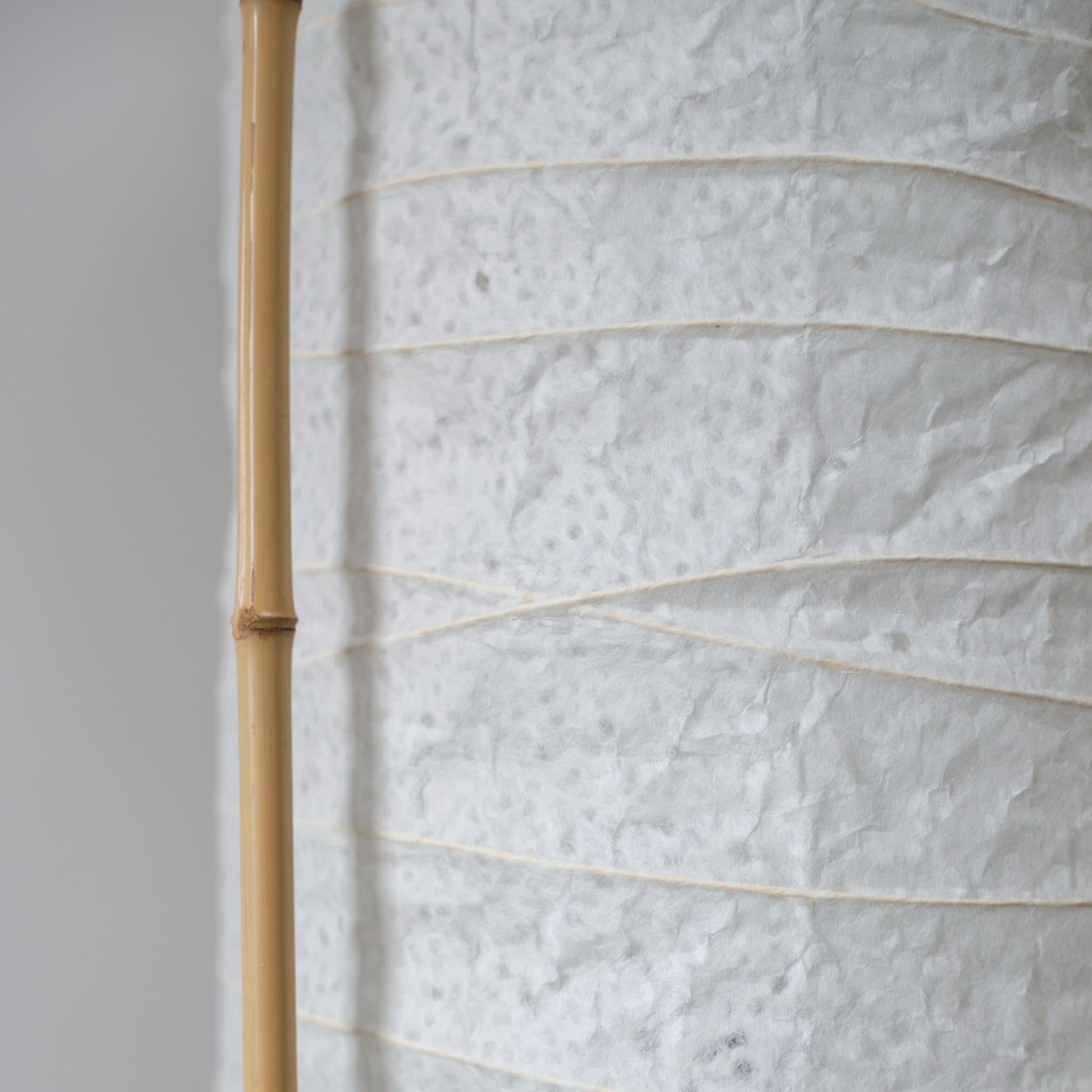Detailed side view of a cylindrical Japanese lamp, showing the contrast between soft white washi paper and brown bamboo frame