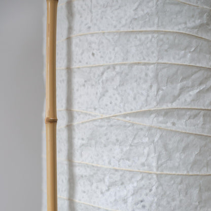 Detailed side view of a cylindrical Japanese lamp, showing the contrast between soft white washi paper and brown bamboo frame