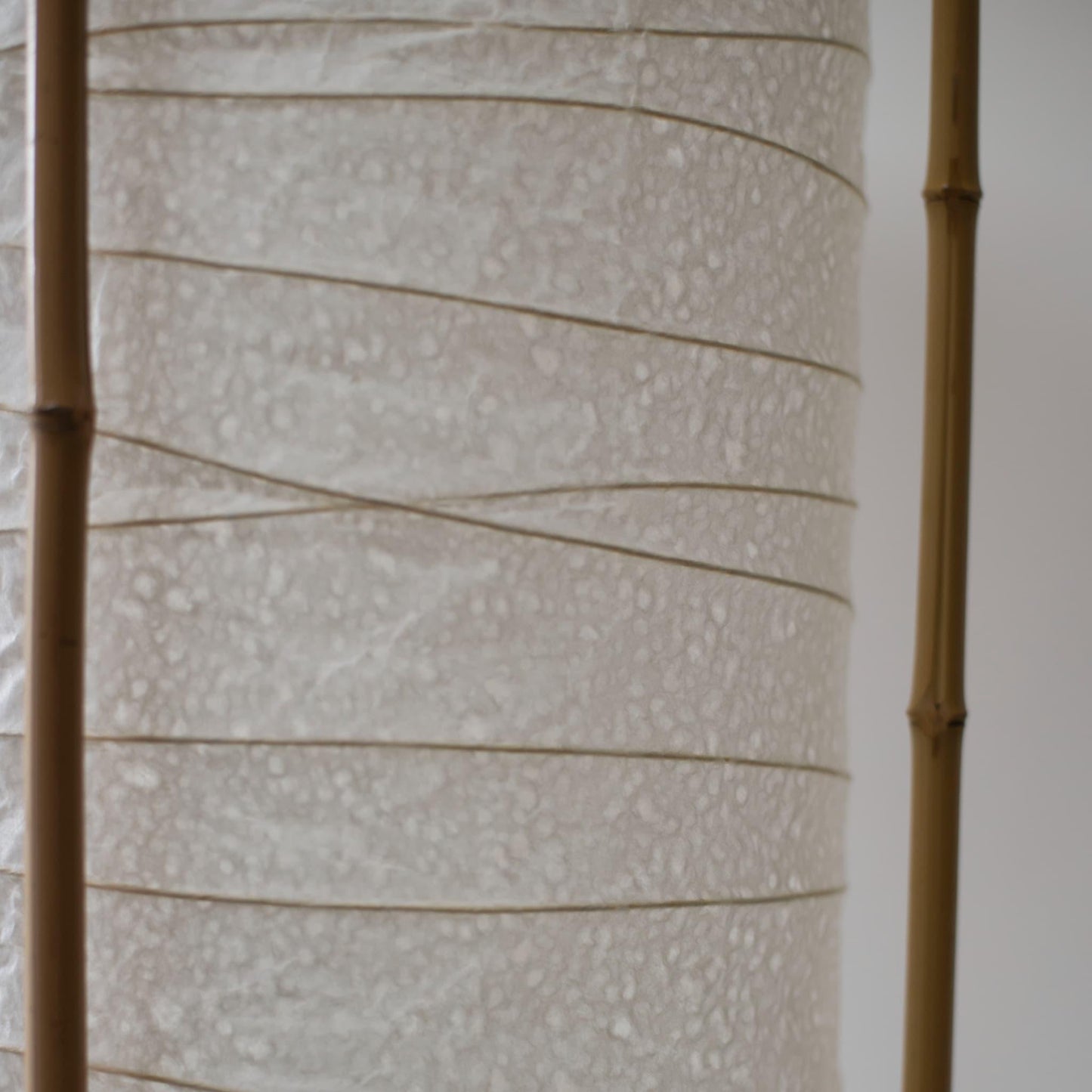 Detailed side view of a cylindrical Japanese lamp, showing the contrast between soft white washi paper and brown bamboo frame