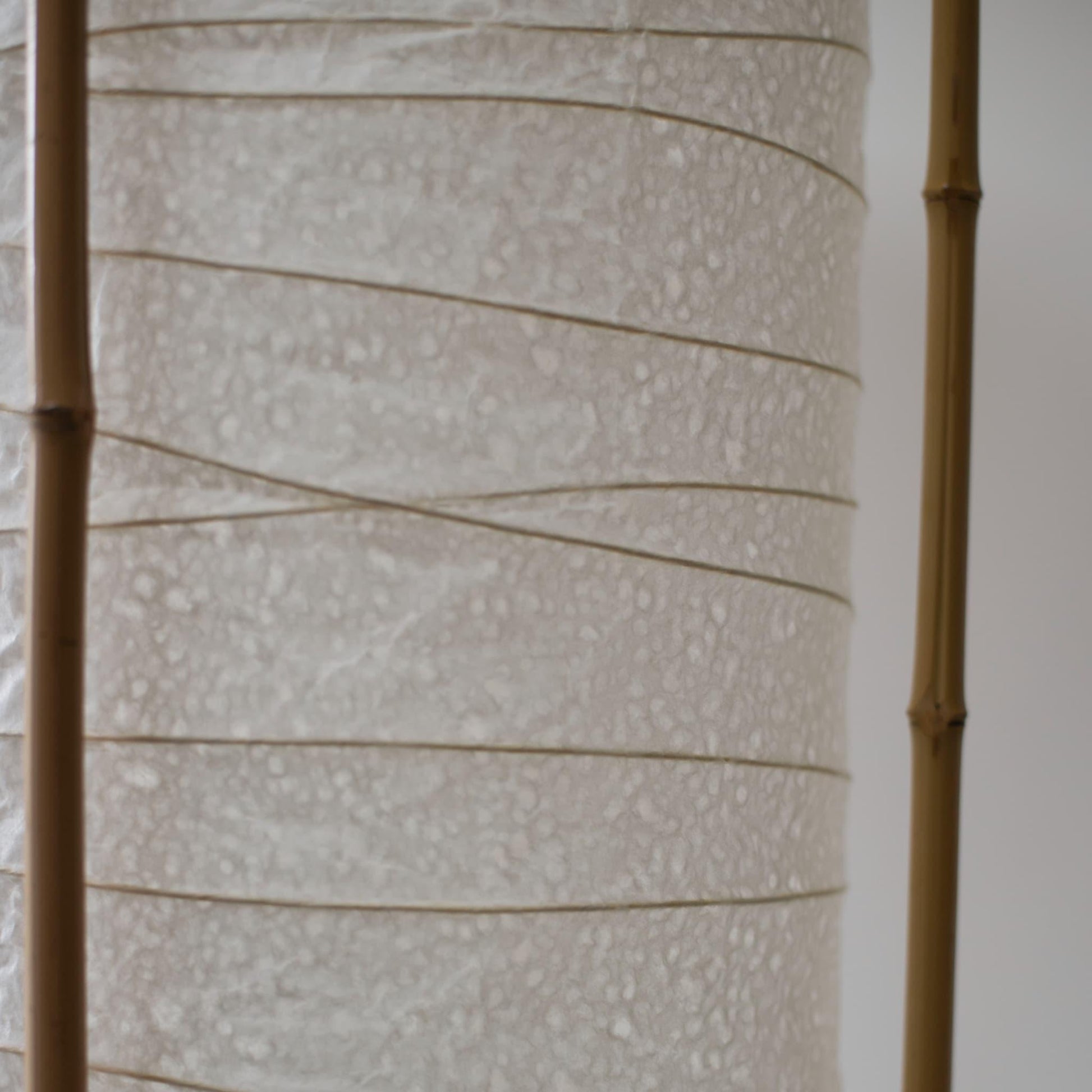 Detailed side view of a cylindrical Japanese lamp, showing the contrast between soft white washi paper and brown bamboo frame