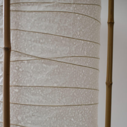 Detailed side view of a cylindrical Japanese lamp, showing the contrast between soft white washi paper and brown bamboo frame