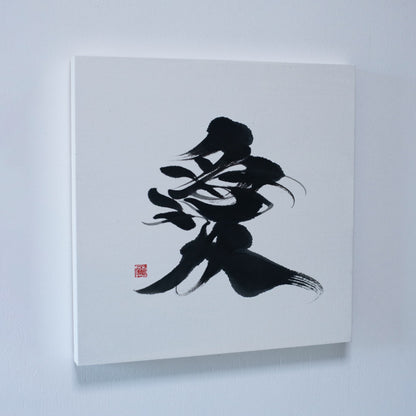 A wall art panel displaying '愛' (love) in Japanese calligraphy, mounted on a white wall. 