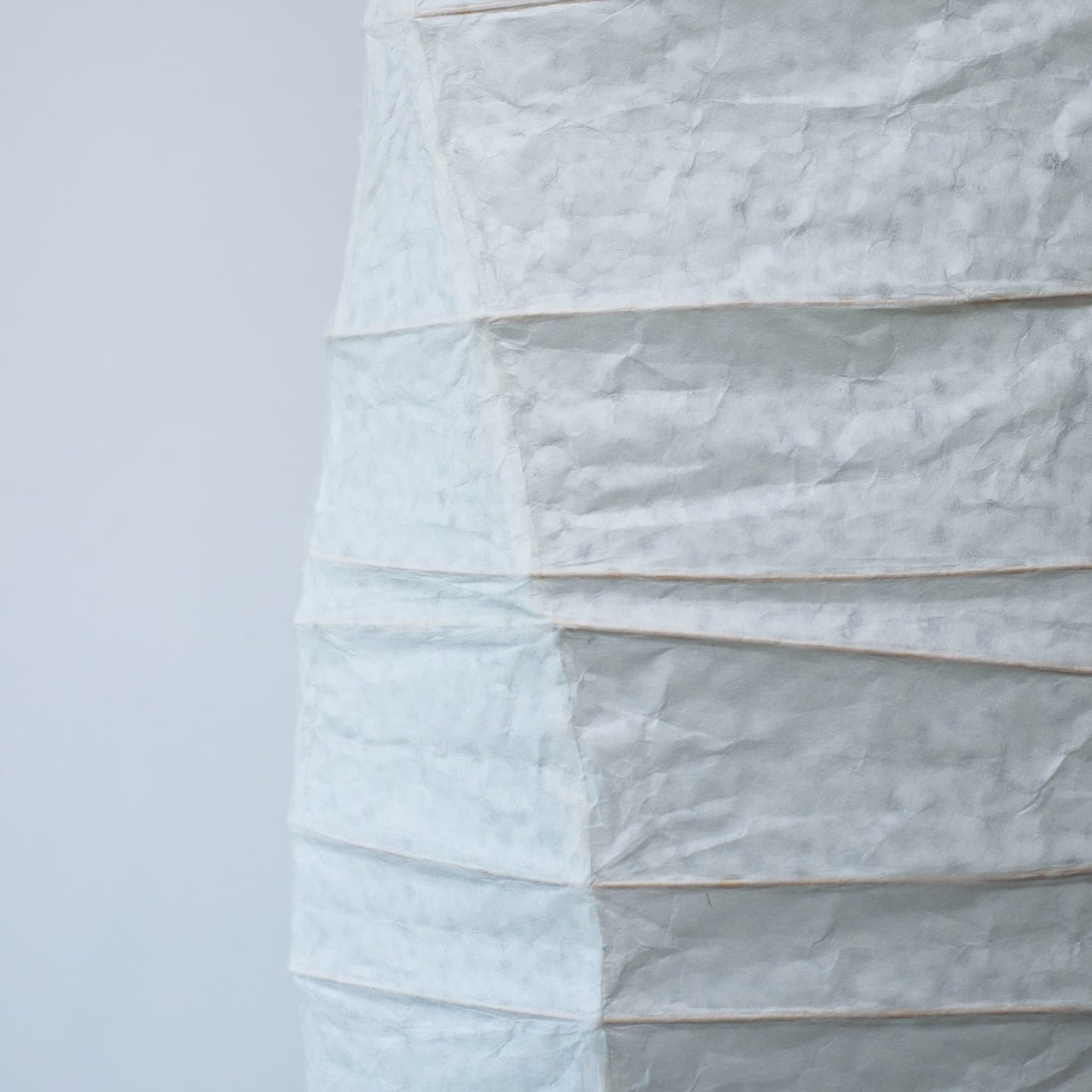 A side view of a Japanese washi paper lamp with flowing curves, highlighting the beauty and texture of the paper on a white background