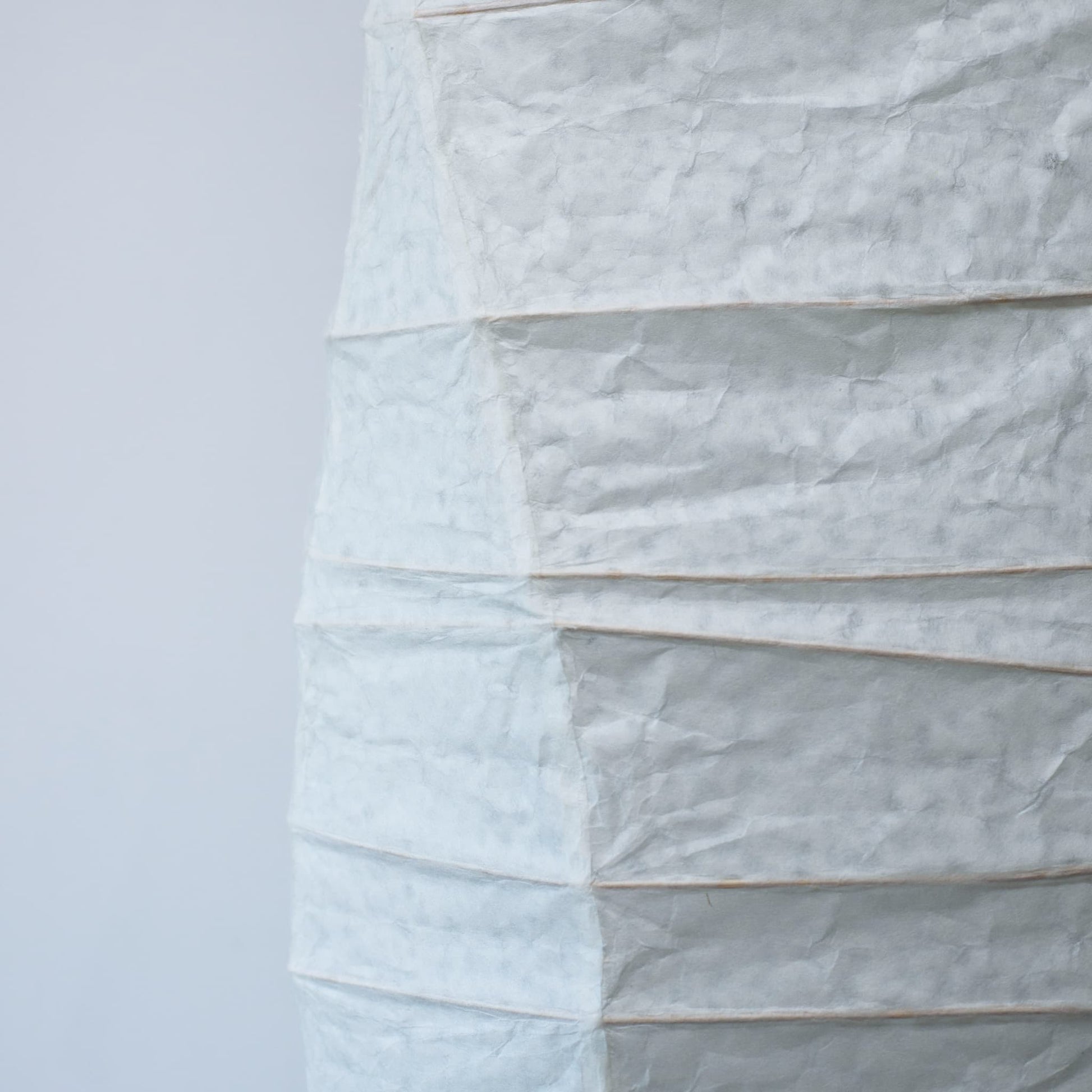 A side view of a Japanese washi paper lamp with flowing curves, highlighting the beauty and texture of the paper on a white background