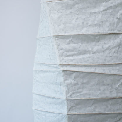 A side view of a Japanese washi paper lamp with flowing curves, highlighting the beauty and texture of the paper on a white background