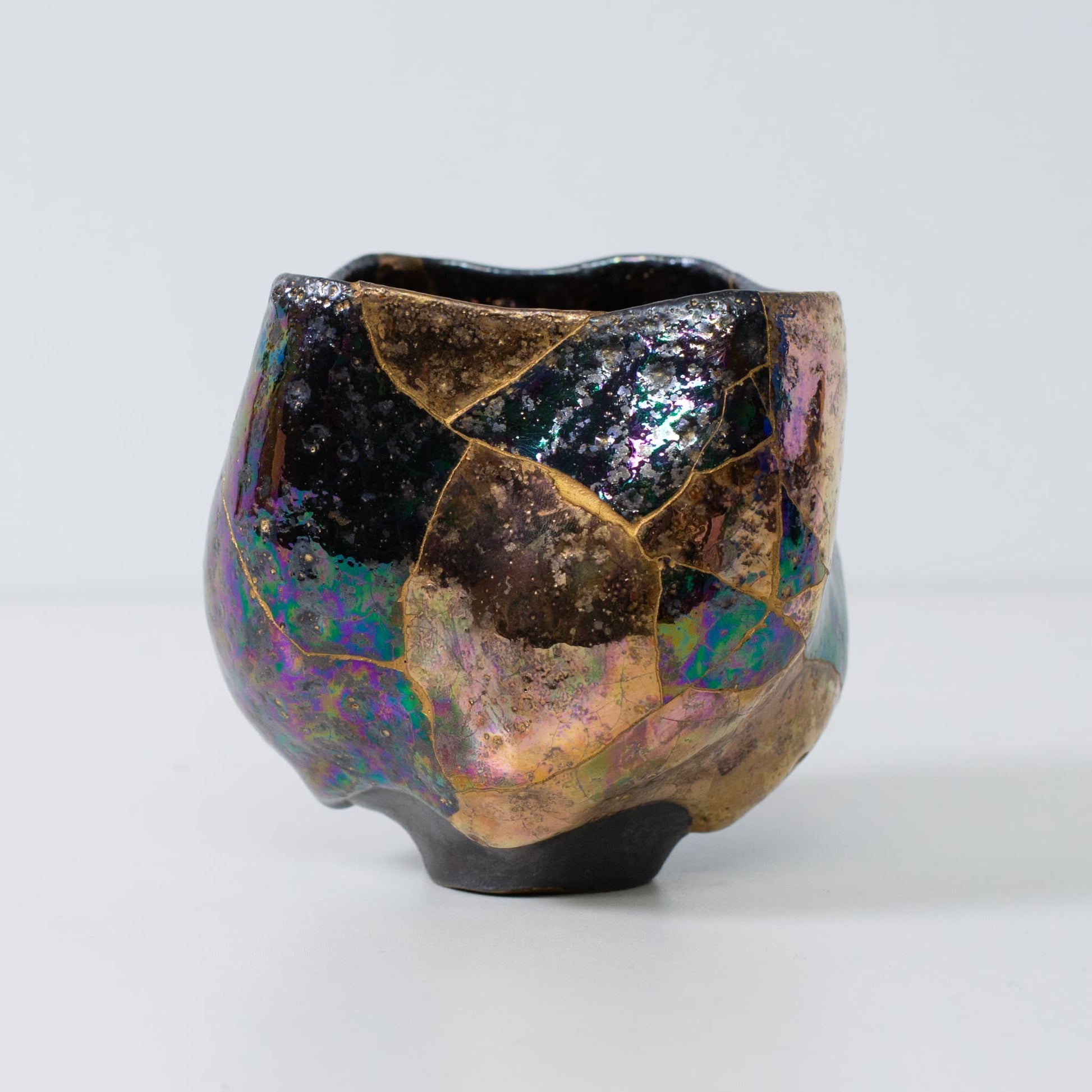 Side view of kintsugi pottery matcha bowl with gold seams and iridescent glaze