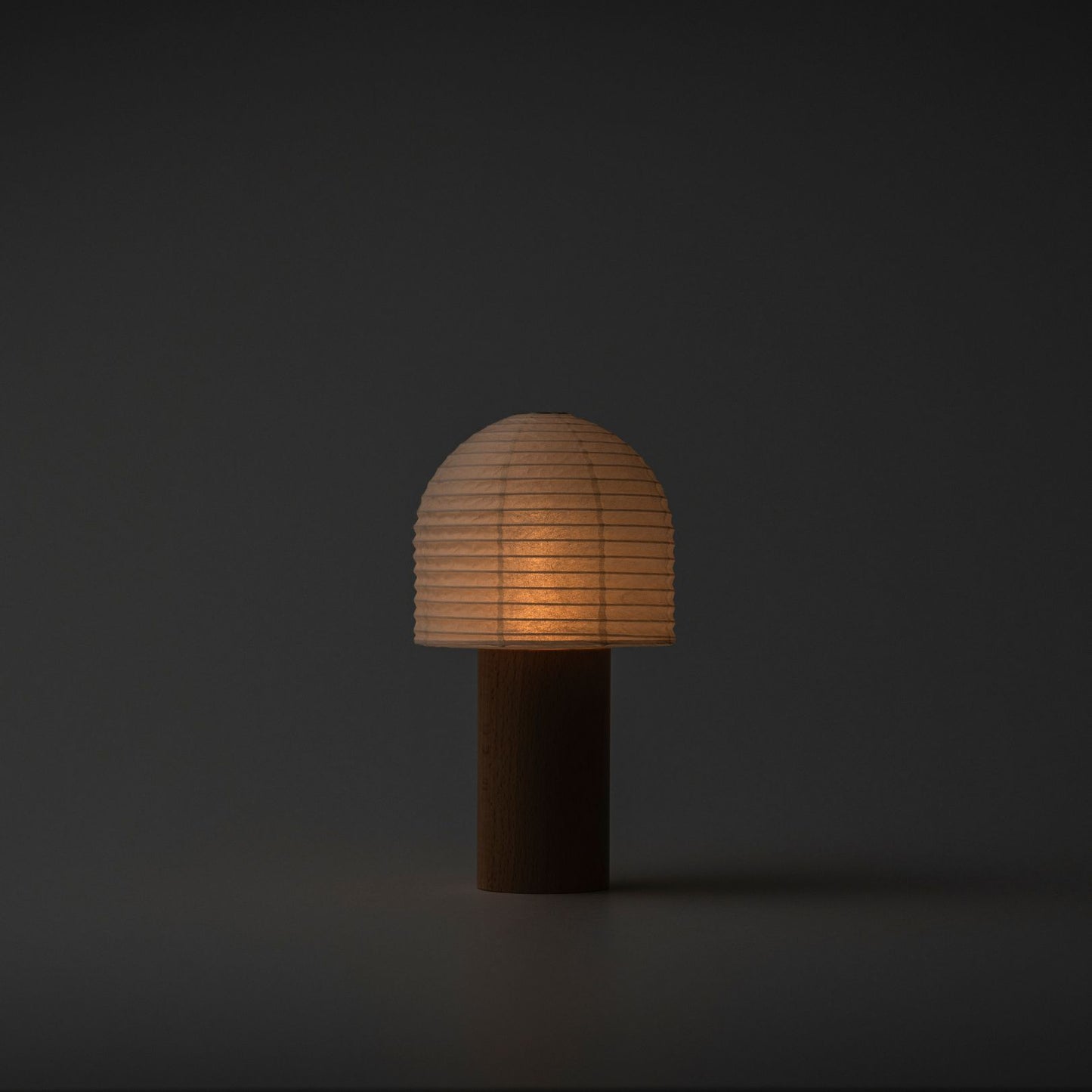 A softly glowing Yame lantern with a bell-shaped top and wooden handle in a dark room