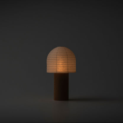 A softly glowing Yame lantern with a bell-shaped top and wooden handle in a dark room