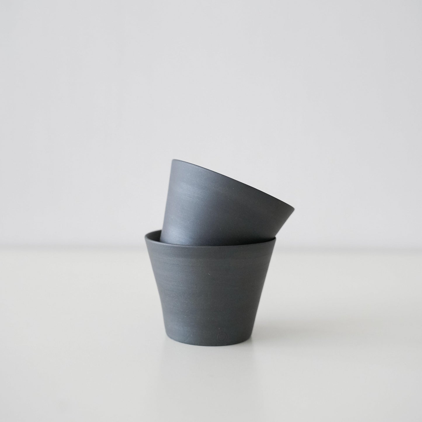 Two simple black conical teacups made of traditional Banko ware stacked together.