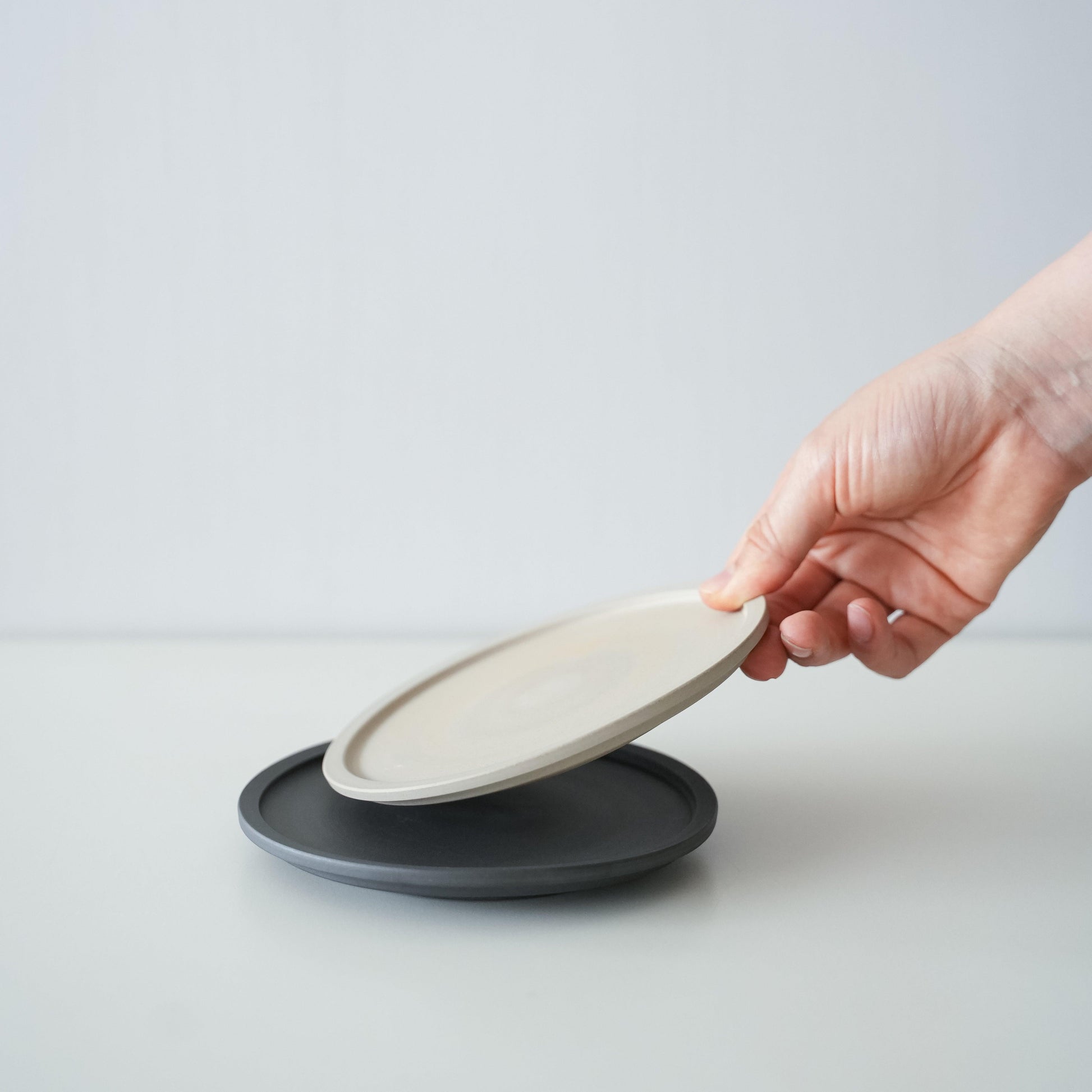 A hand stacking a white plate on a simple black Banko ware plate.