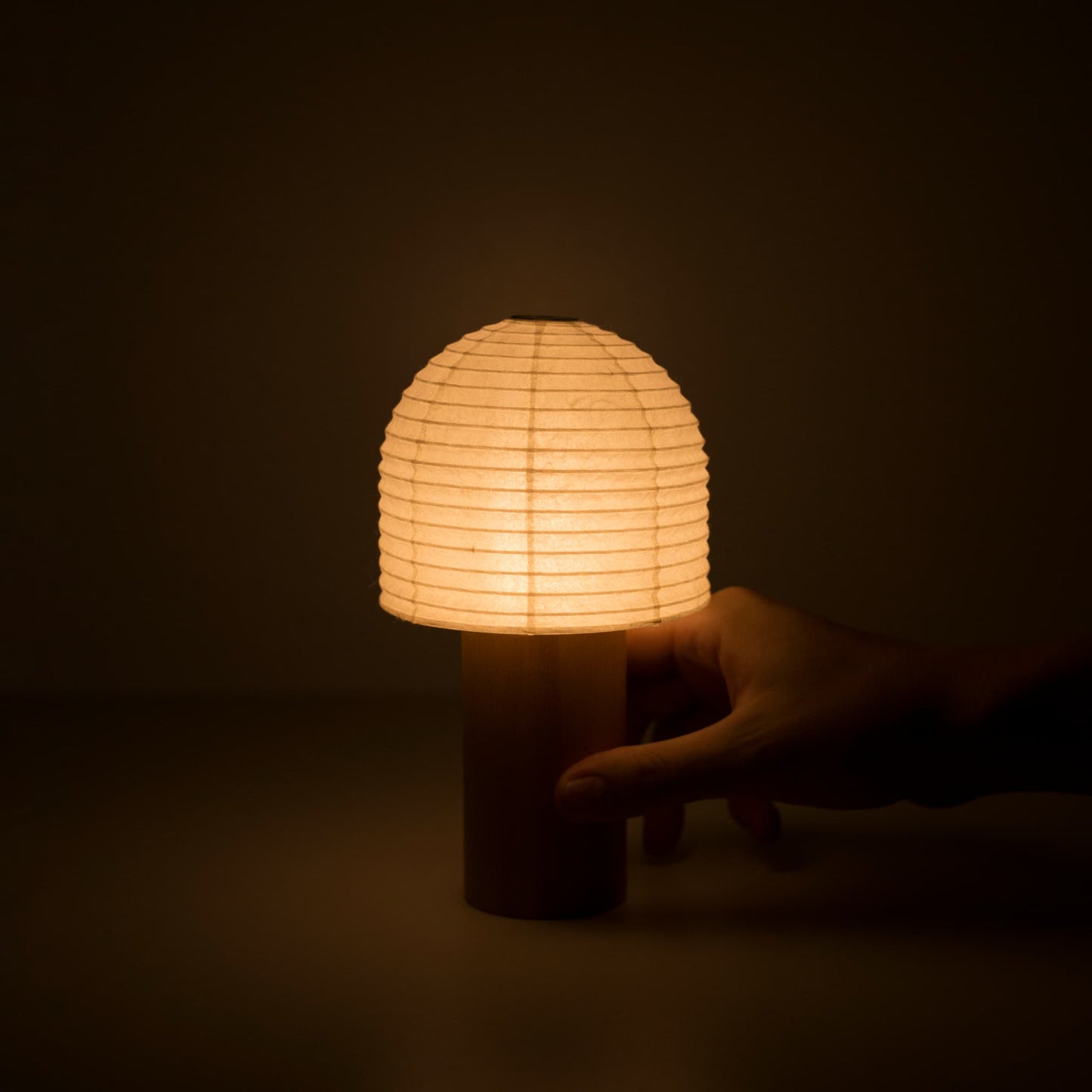 A hand holding a warmly glowing Yame lantern in a dark room