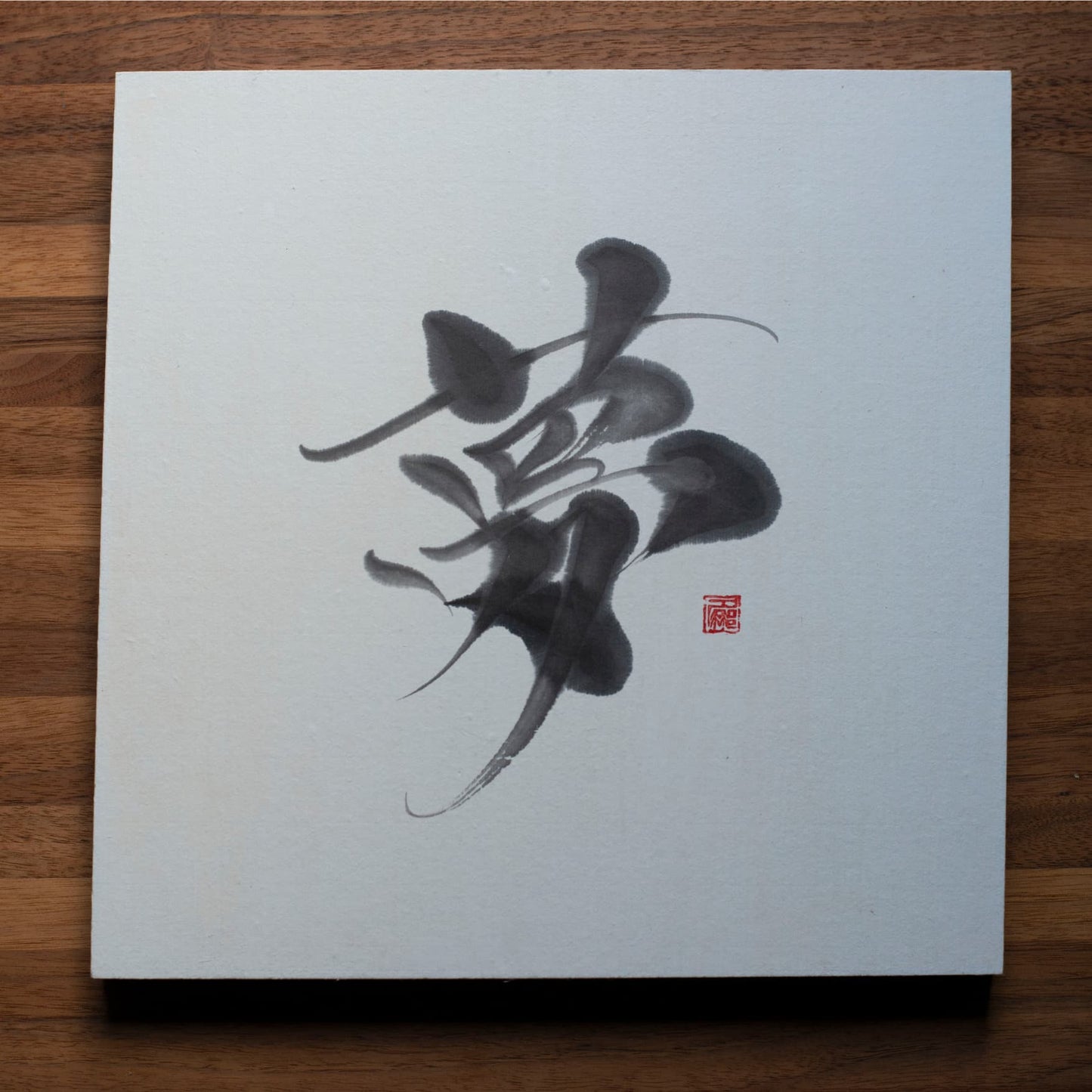 A top-down photo of a square panel with the Japanese character for "dream" (夢) written in calligraphy, placed on a wooden table.