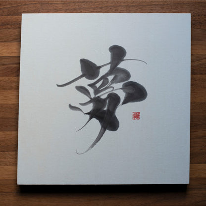 A top-down photo of a square panel with the Japanese character for "dream" (夢) written in calligraphy, placed on a wooden table.