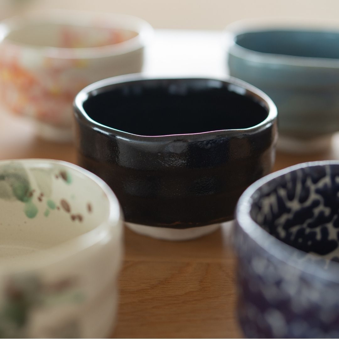 Five diverse Mino Ware Japanese matcha chawan bowls, featuring a central dark black bowl, and others with colorful glazes and patterns, ideal for tea ceremony.