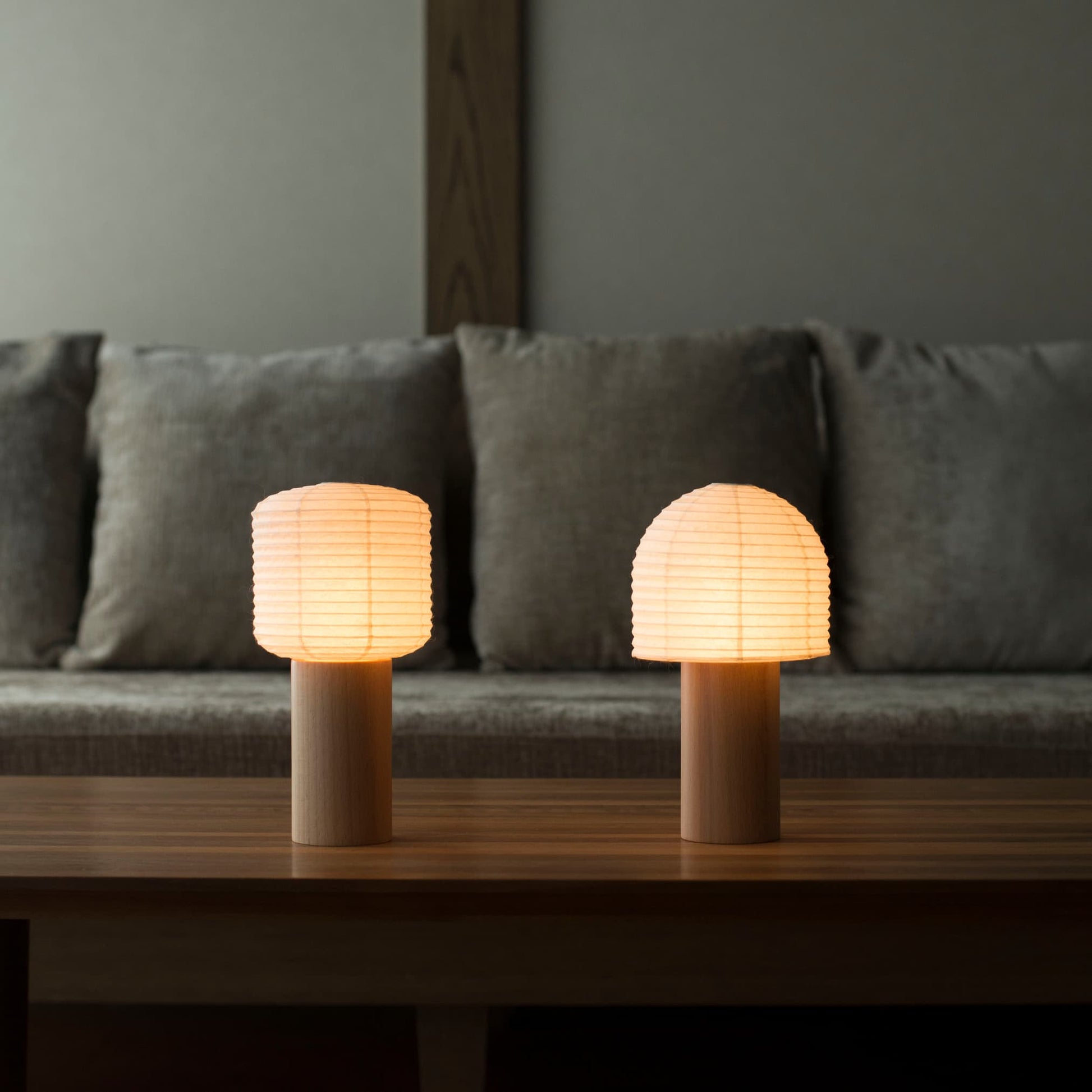 Two portable Japanese paper lamps with warm light, placed on a table in a traditional Japanese-style room.