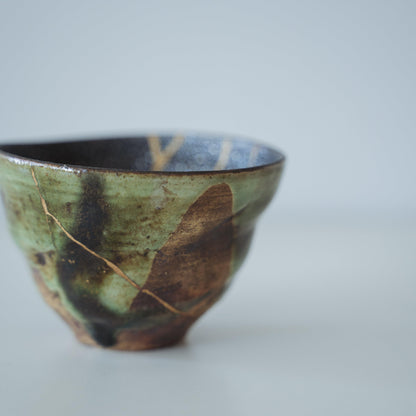 Deep green tea bowl repaired with Kintsugi, a traditional Japanese technique, showcasing the beauty of imperfection.