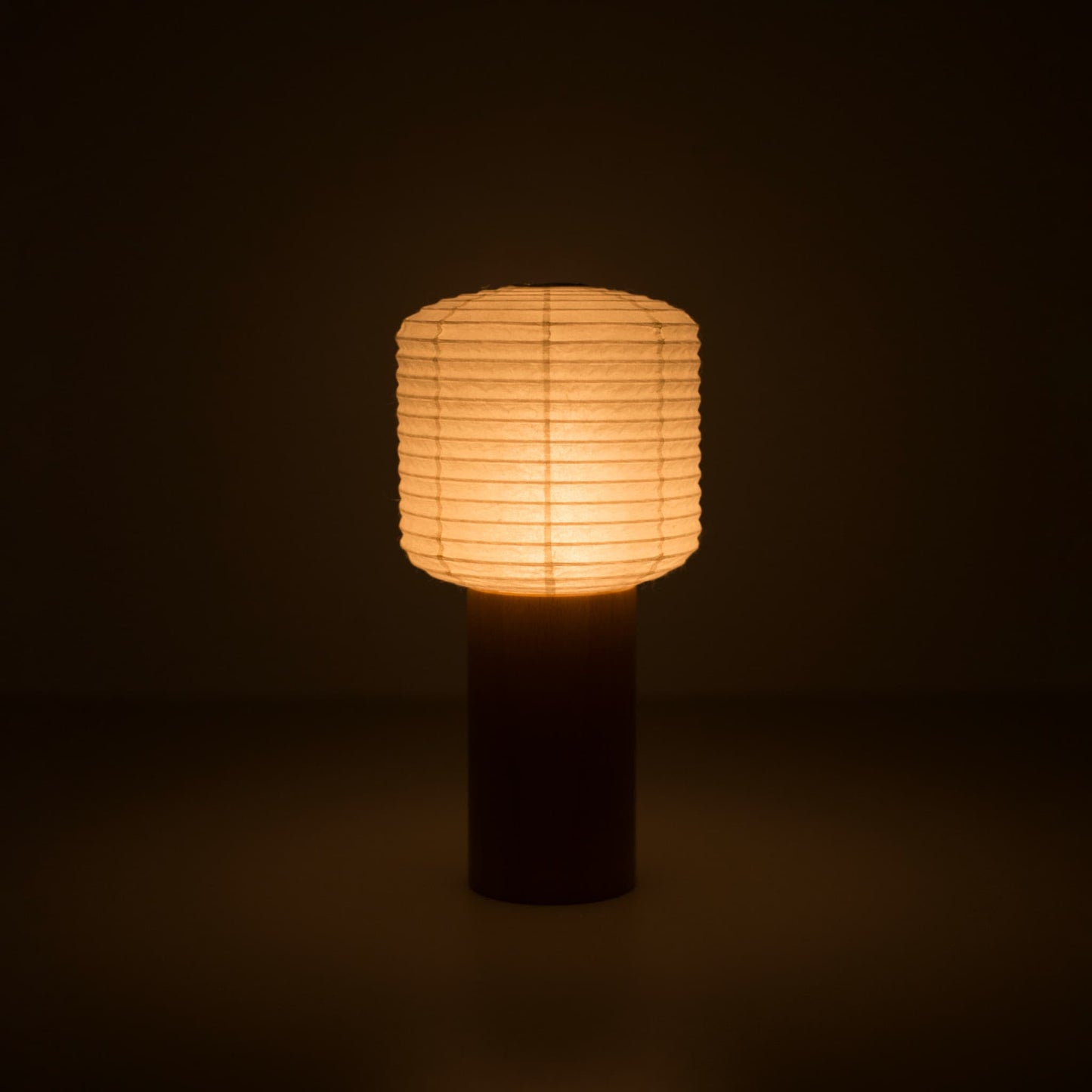 A portable paper lamps with a small paper lantern top and wooden handle, glowing warmly in a dark room