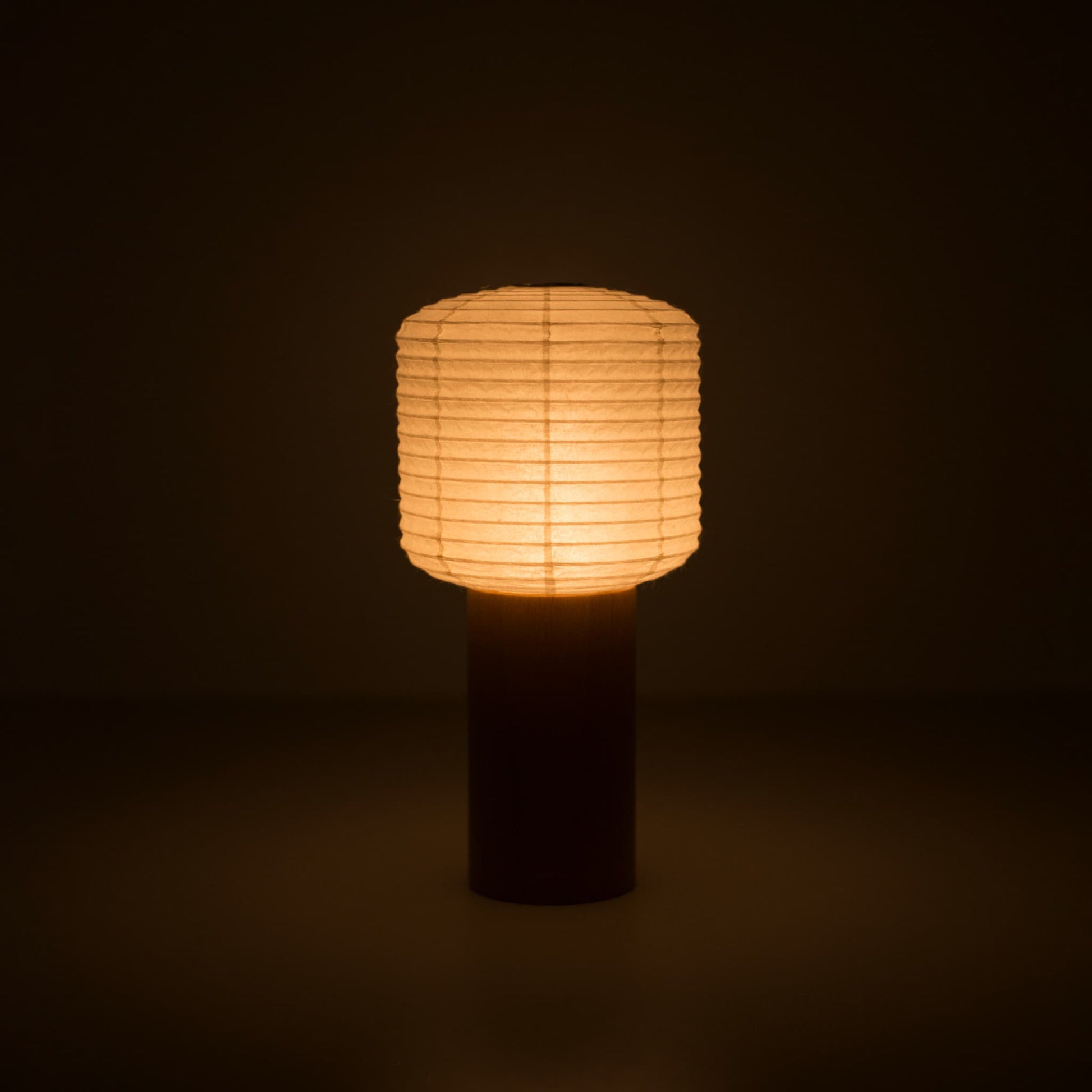 A portable paper lamps with a small paper lantern top and wooden handle, glowing warmly in a dark room