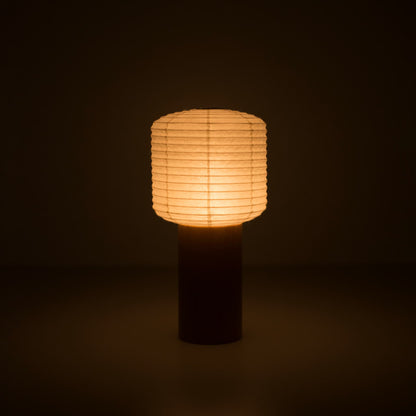 A portable paper lamps with a small paper lantern top and wooden handle, glowing warmly in a dark room