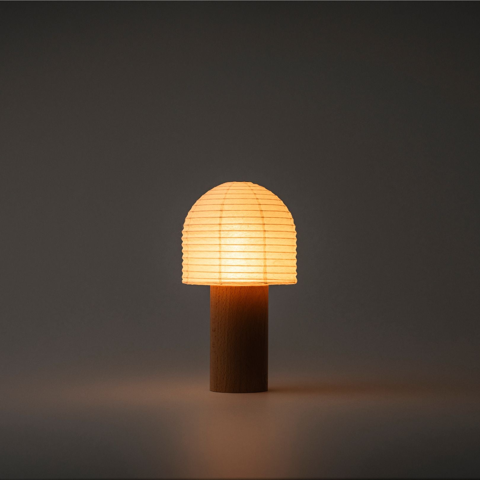 A Yame lantern with a bell-shaped top and wooden handle, emitting bright warm light in a dark room