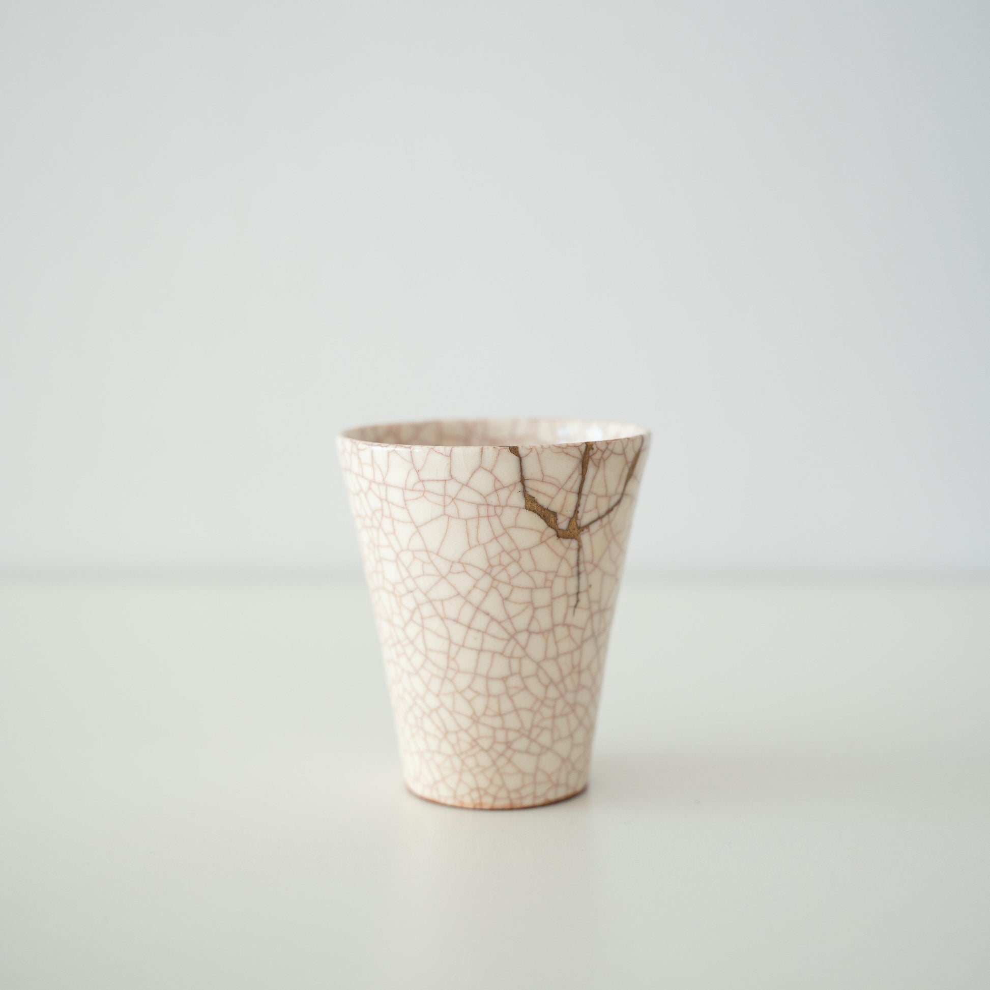 White ceramic cup repaired with kintsugi, a traditional Japanese art of mending broken pottery with gold lacquer, showcasing the beauty of imperfection and embracing the concept of wabi-sabi.