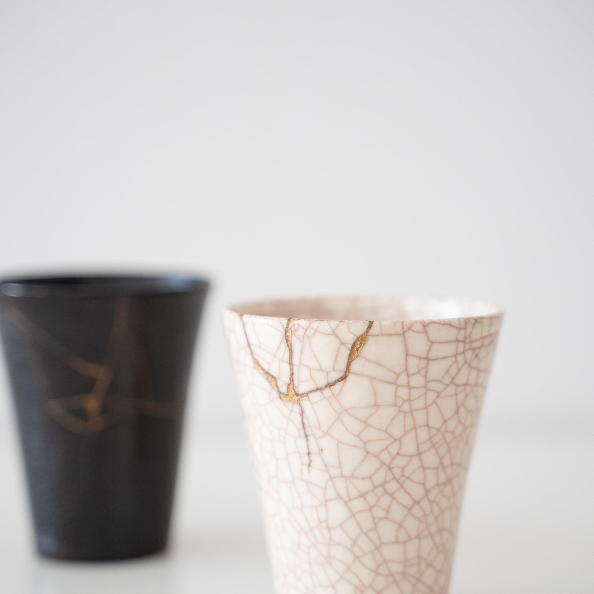 White and black ceramic cups repaired with kintsugi, a traditional Japanese art of mending broken pottery with gold lacquer, showcasing the beauty of imperfection and embracing the concept of wabi-sabi.