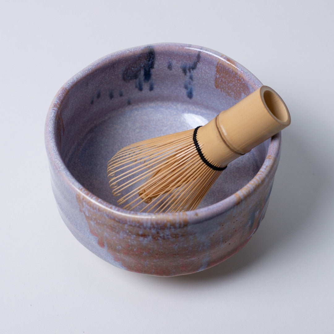 Top view of "Navy & Red Splash" matcha chawan bowl with a bamboo whisk, showcasing the unique fusion of purple, navy, and red kiln-fired patterns.