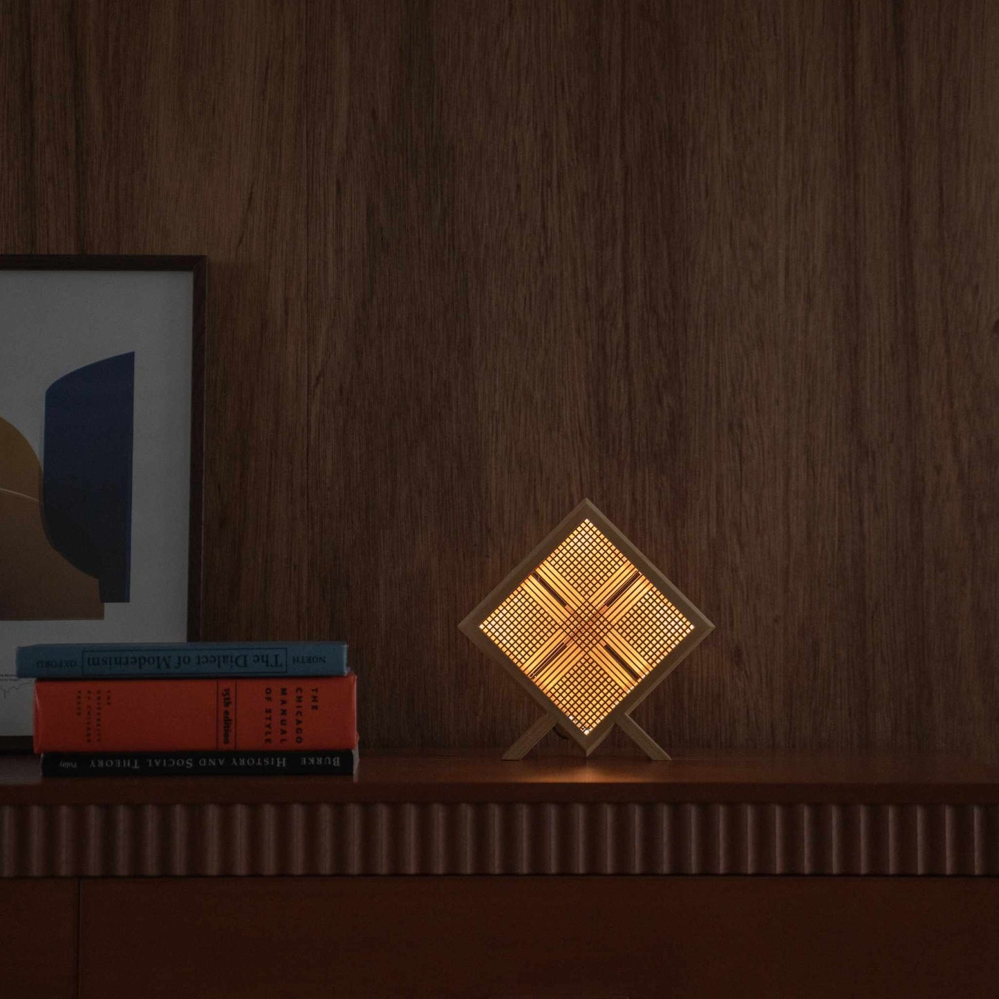 "Lampe de table japonaise en bois Lit « Kanata » servant de lampe d'ambiance, projetant une œuvre d'art en forme de X sur une console de style mid-century modern."