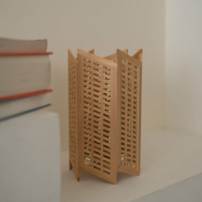 Gros plan d'une lampe de table japonaise en bois "Towaru" à côté de livres, présentant un travail complexe du bois Kumiko sur une lampe en bois.