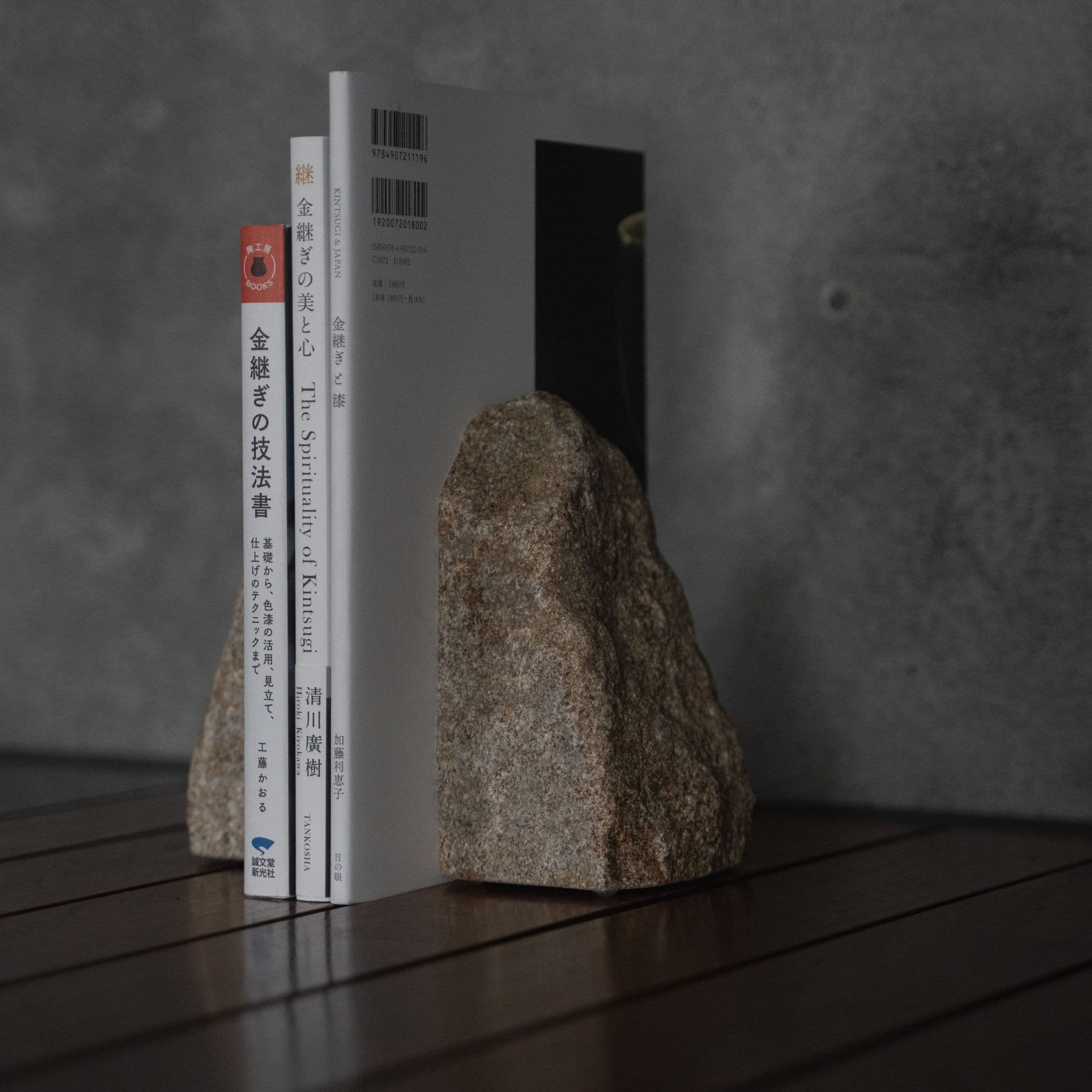A premium Aji stone bookend displayed on a wooden table against a textured grey hotel wall backdrop.