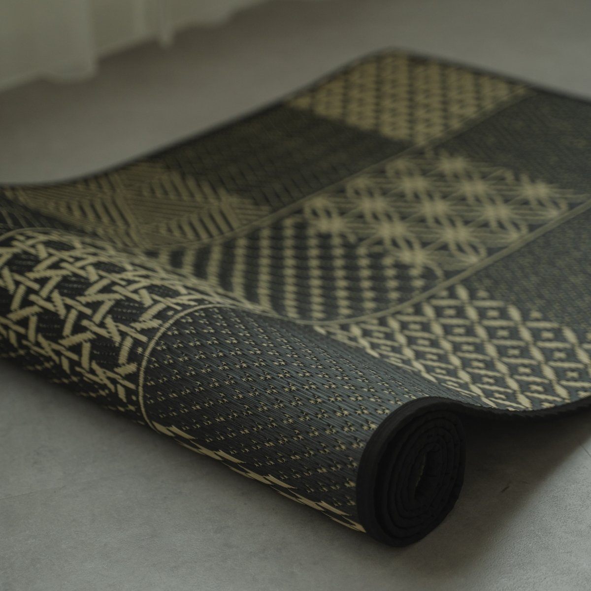 Japanese Tatami Yoga Mattress "Ed Plain" Black partially rolled, displaying the traditional Edo Komon woven pattern.