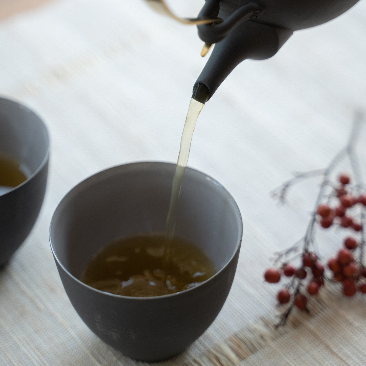 Serving tea from a black kyusu into Japanese tea cups in a bright room for hosts creating a wabi sabi atmosphere.
