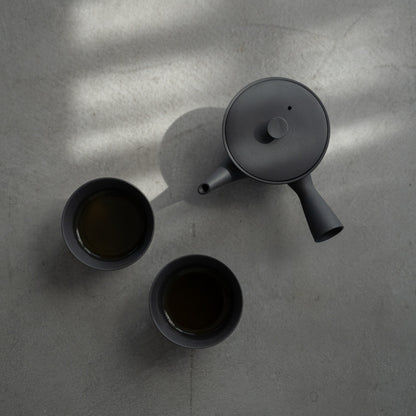 Black kyusu "Sencha" and filled Japanese tea cups on a concrete surface for minimalists enjoying a quiet tea break.