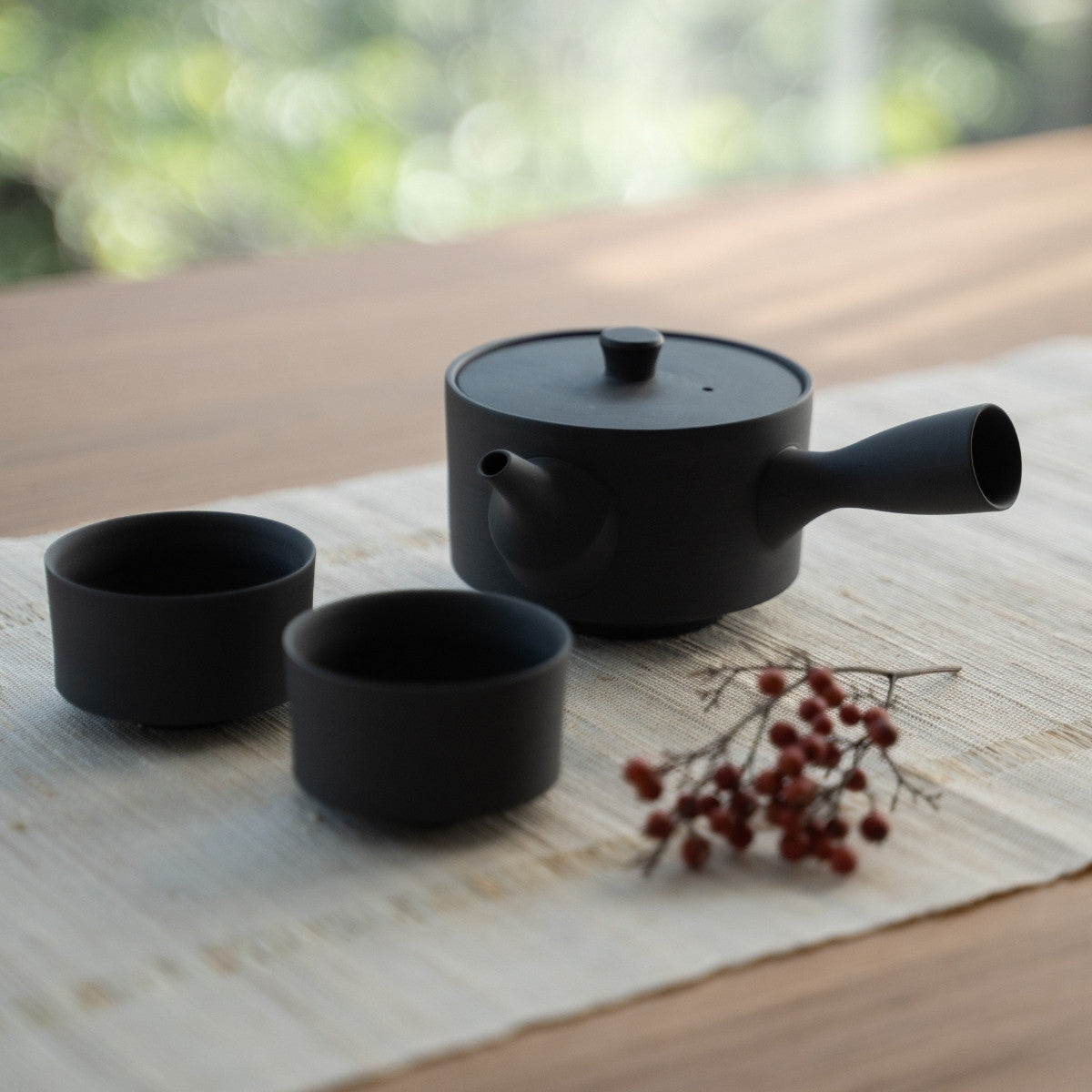 Théière japonaise noire et tasses à thé japonaises sur un tapis en lin pour les amateurs de thé, créant une esthétique moderne et sereine.