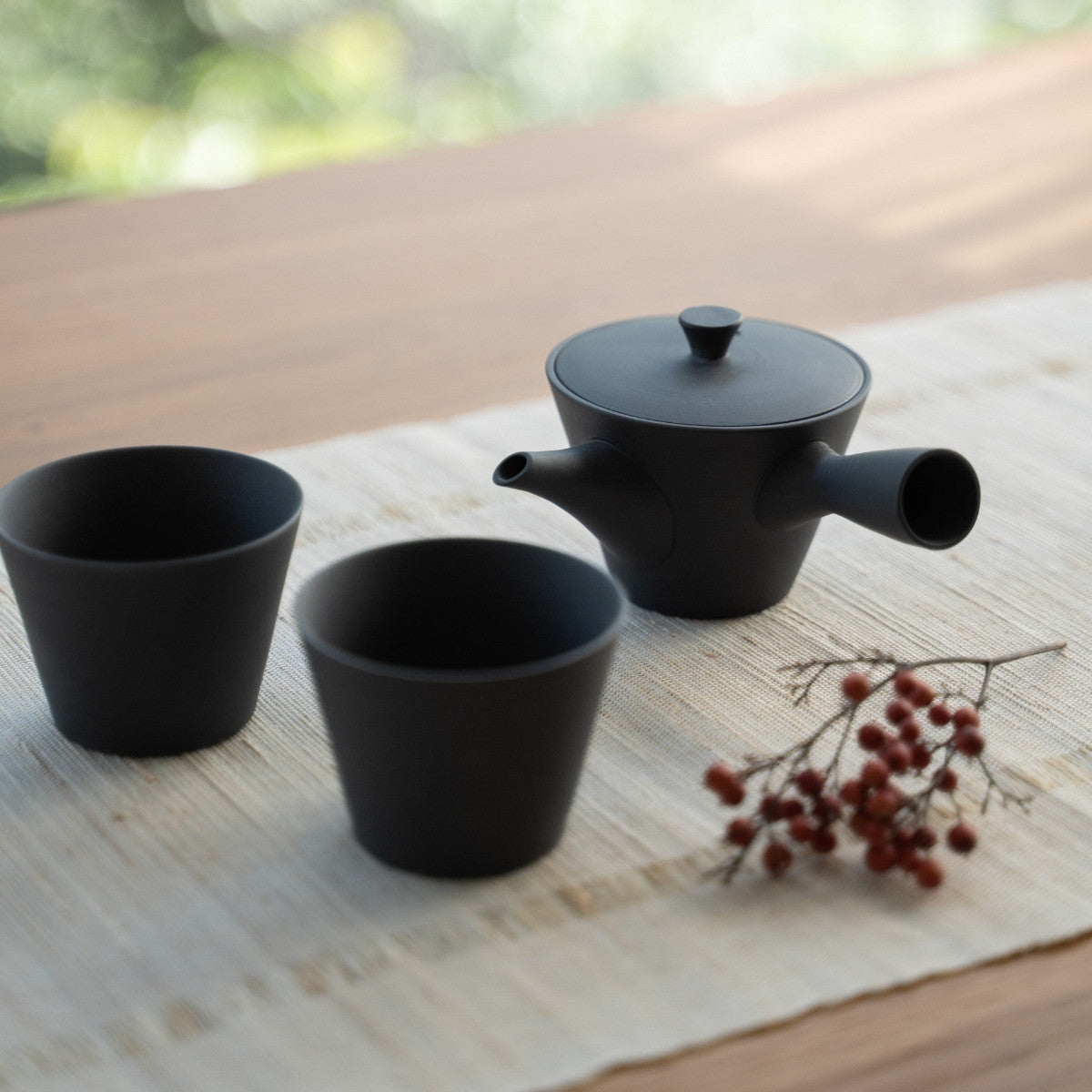 Black Japanese teapot "Sencha" and cone cups on a linen runner for tea enthusiasts preparing a serene brew.