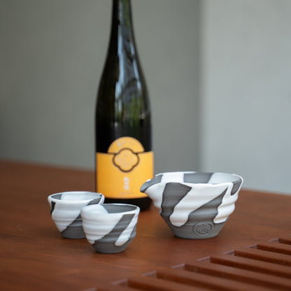 Weißes Flow Sake-Set aus Japan, Karaffe und Becher auf einem Holztisch neben einer Sake-Flasche, für besondere Abendessen mit Gästen