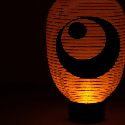 Close-up of the hand-painted black ink moon motif on a glowing washi paper lantern in a dark setting.