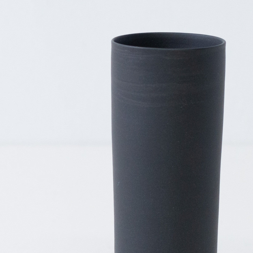 Close up of a textured matte black Japanese flower vase showing handcrafted trowel marks on unglazed stoneware.