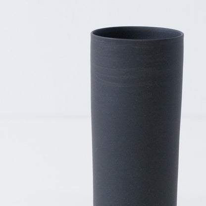 Close up of a textured matte black Japanese flower vase showing handcrafted trowel marks on unglazed stoneware.