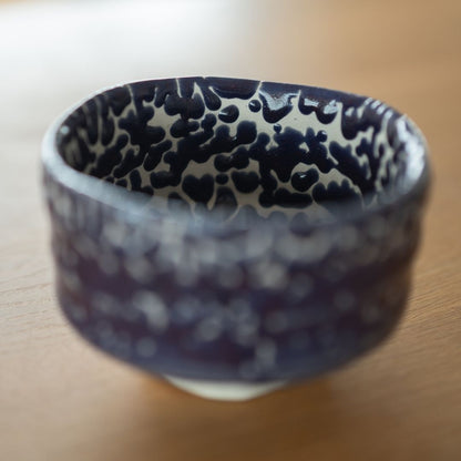 Close-up view of the interior of a Japanese matcha bowl, featuring the dark 'Midnight Blue' Kairagi glaze pattern against a white base, highlighting the wabi sabi cracked texture.