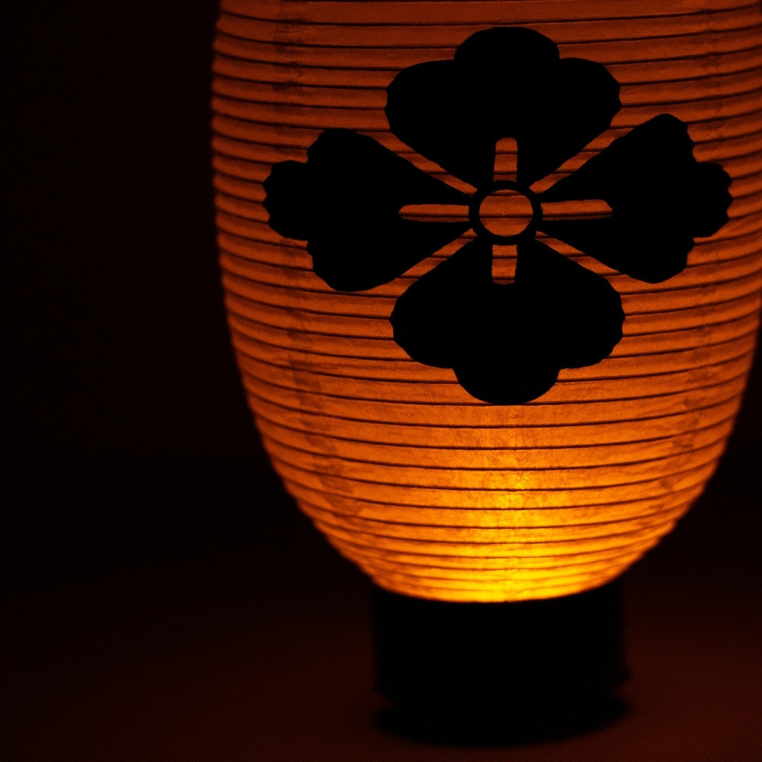 Close-up of a hand-painted black flower diamond crest on the textured surface of an illuminated washi paper lantern.