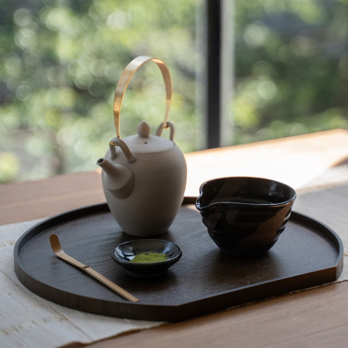 Sumi Black Spouted Japanese Matcha Bowl and Teapot, on a wooden tray by a sunlit window, ready for a modern matcha latte ritual.